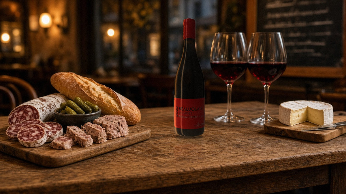 Garrafa de L'Arlésienne Beaujolais-Villages Aux Gauthiers 2022 numa mesa de bistrô com charcutaria, queijo e dois copos de vinho tinto